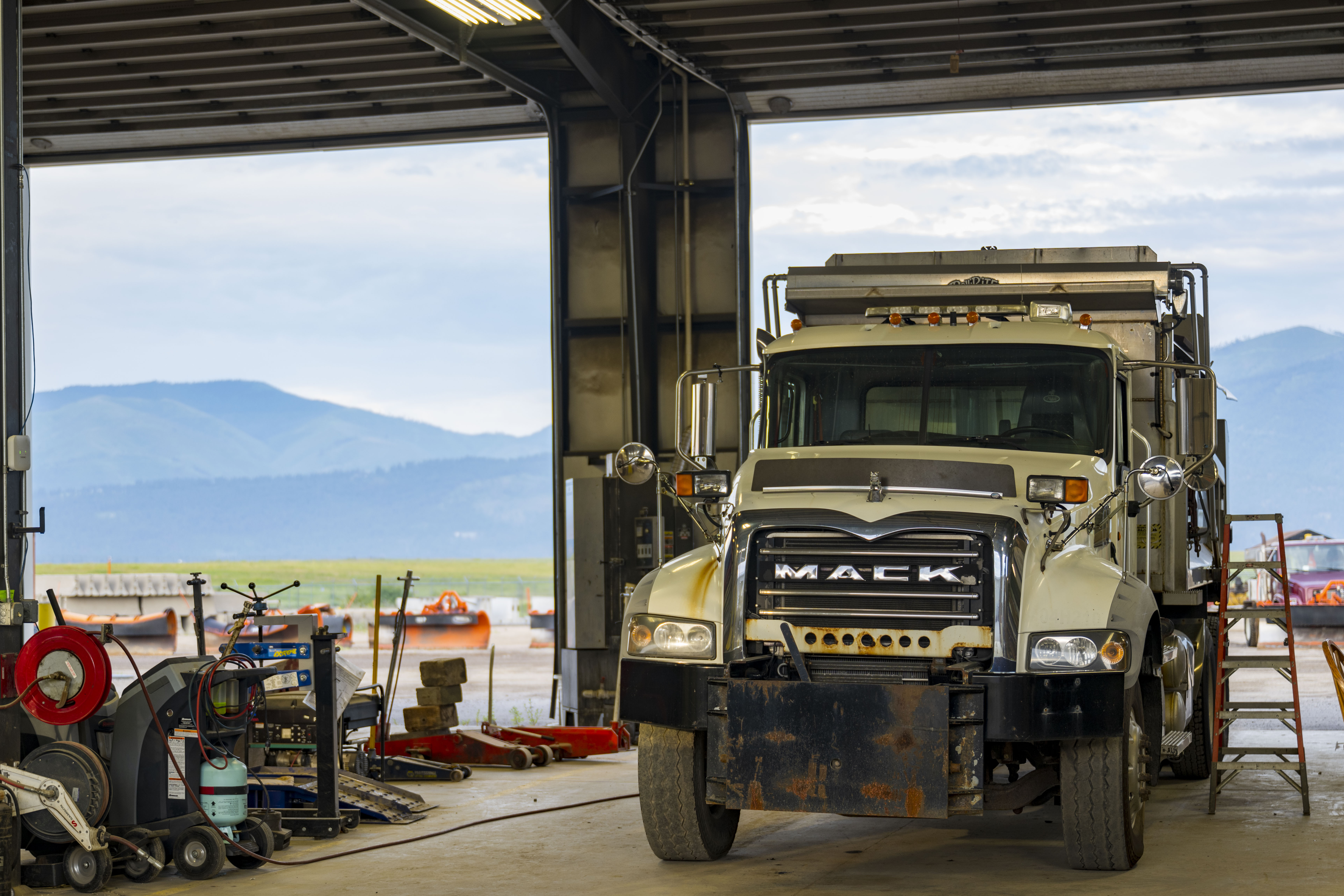 A Mack truck in the Public Works shop, with mountains visible in the background